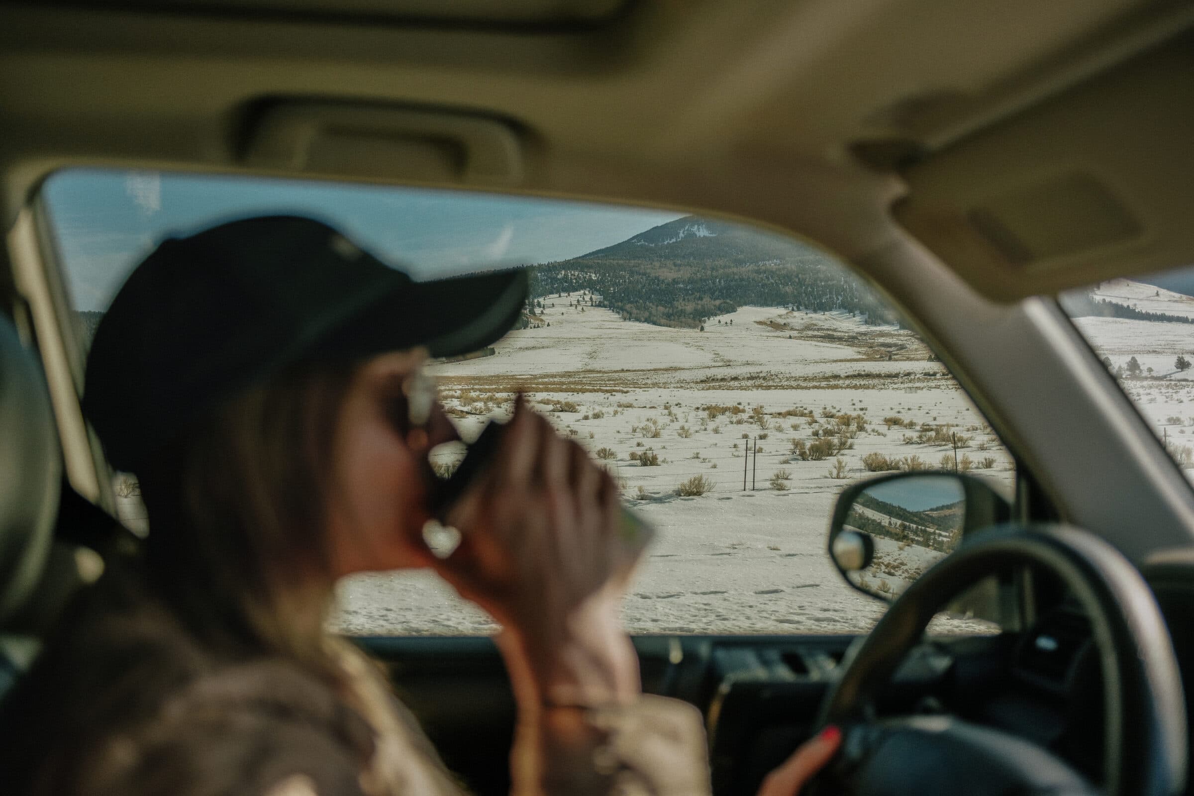 woman drinking coffee while driving with mountain view outside the window