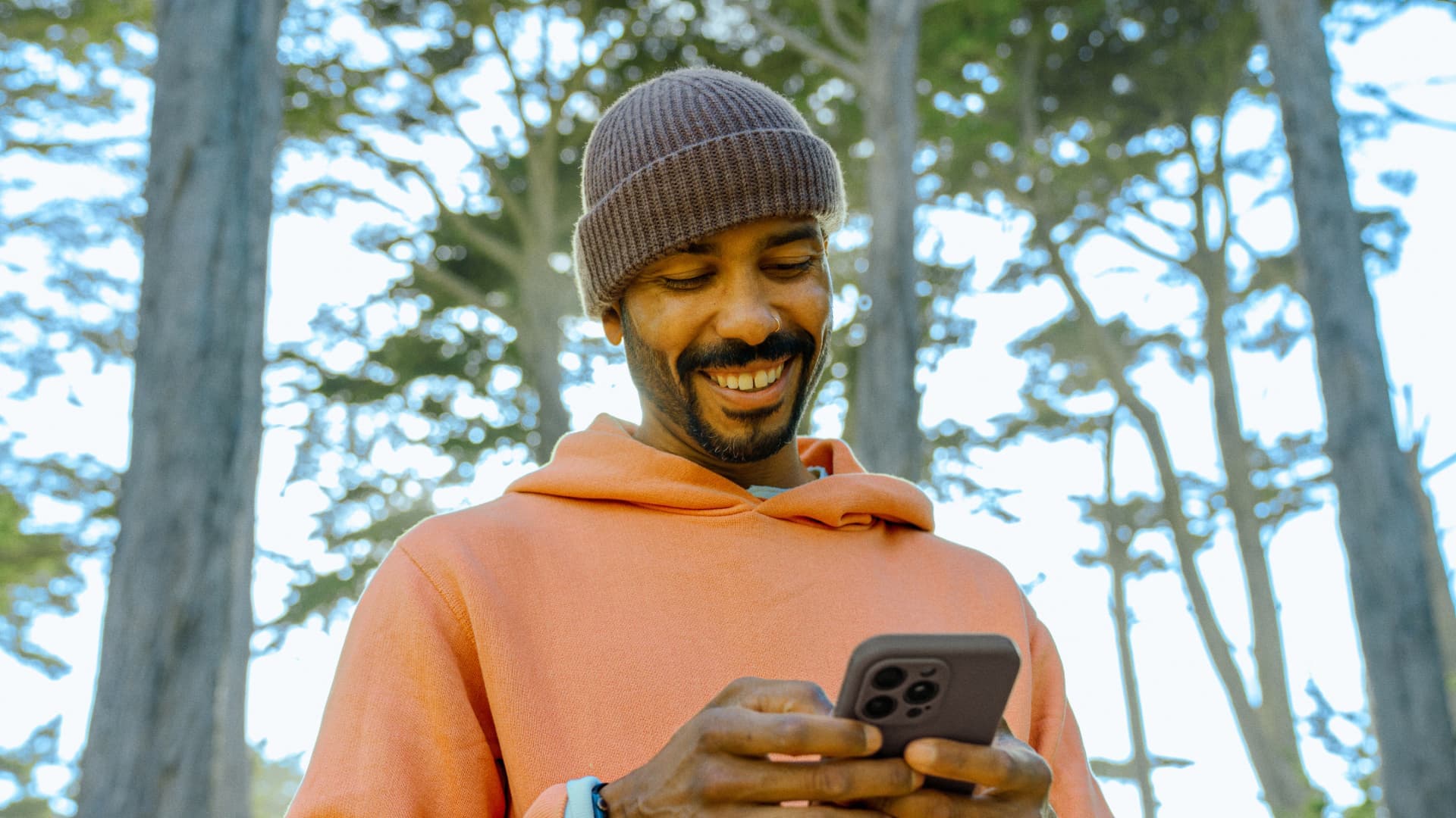 man in an orange hoodie using his phone in a forest